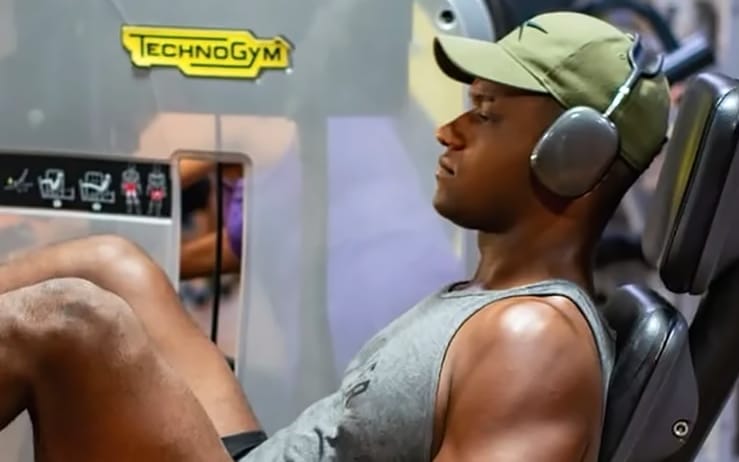 Felipe Mota de boné e fones de ouvido em um treino de pernas na leg press